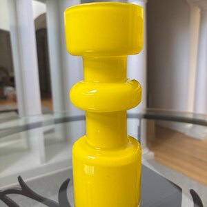 Peut inclure: Un vase en verre jaune vif au design g&eacute;om&eacute;trique unique. Le vase pr&eacute;sente une base cylindrique, une section m&eacute;diane arrondie et un dessus rectangulaire. La finition brillante refl&egrave;te la lumi&egrave;re, soulignant la couleur vibrante. Id&eacute;al pour la d&eacute;coration int&eacute;rieure.