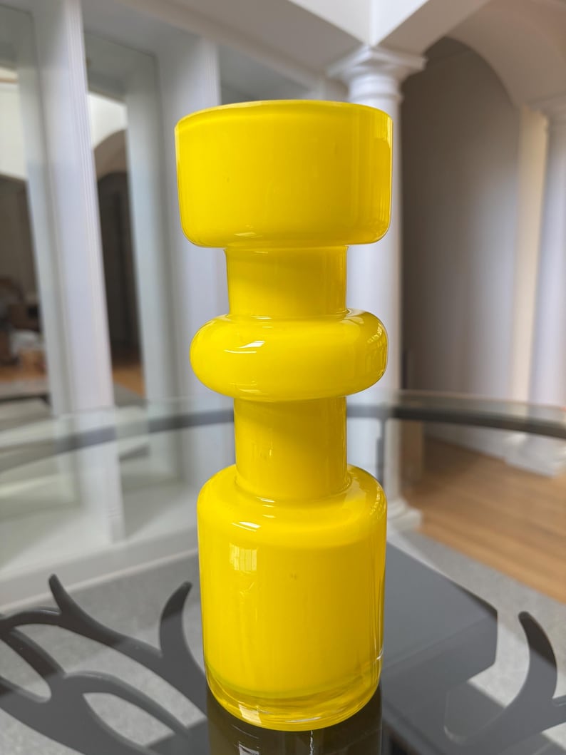 Peut inclure: Un vase en verre jaune vif au design g&eacute;om&eacute;trique unique. Le vase pr&eacute;sente une base cylindrique, une section m&eacute;diane arrondie et un dessus rectangulaire. La finition brillante refl&egrave;te la lumi&egrave;re, soulignant la couleur vibrante. Id&eacute;al pour la d&eacute;coration int&eacute;rieure.