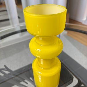 Peut inclure: Un vase en verre jaune vif avec une base arrondie, une section m&eacute;diane bomb&eacute;e et un large sommet ouvert. Le vase est fait d'un mat&eacute;riau brillant et opaque et repose sur une table en verre. Le design rappelle le d&eacute;cor moderne du milieu du si&egrave;cle.