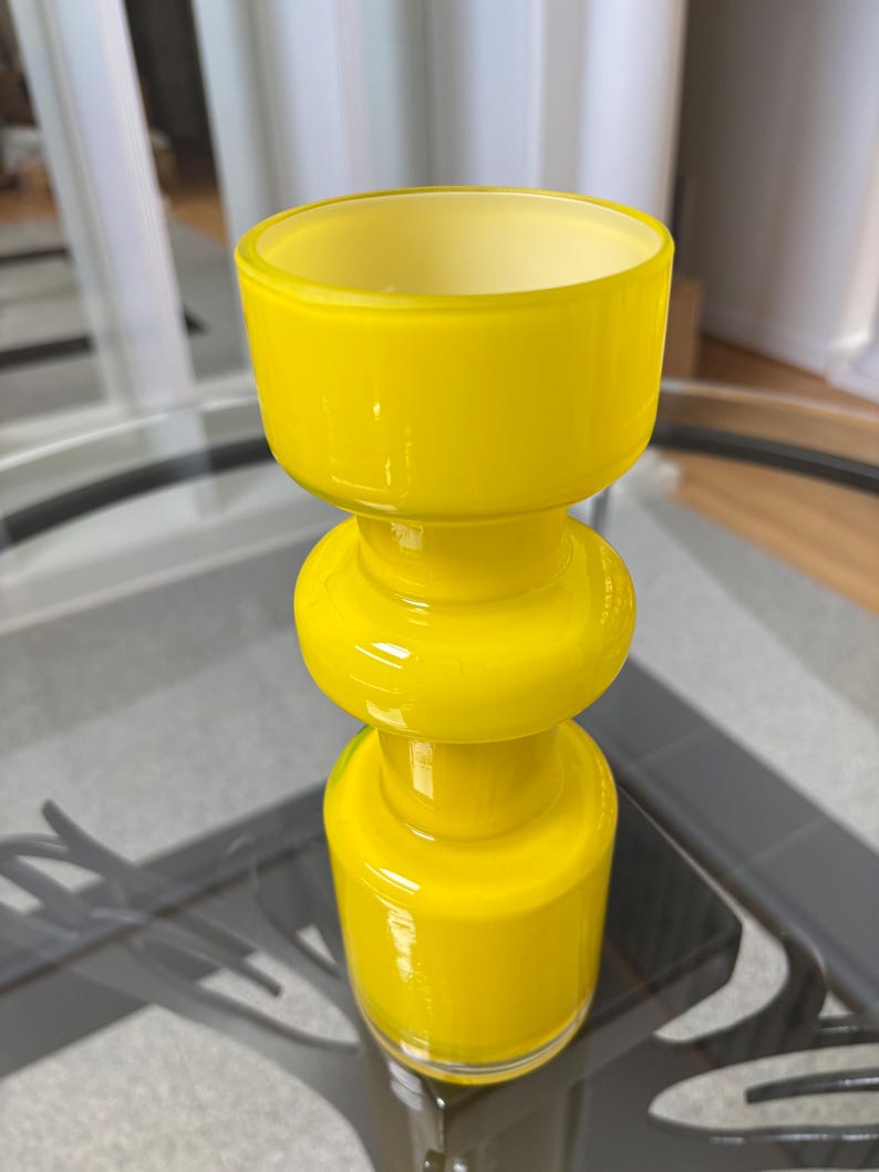 Peut inclure: Un vase en verre jaune vif avec une base arrondie, une section m&eacute;diane bomb&eacute;e et un large sommet ouvert. Le vase est fait d'un mat&eacute;riau brillant et opaque et repose sur une table en verre. Le design rappelle le d&eacute;cor moderne du milieu du si&egrave;cle.