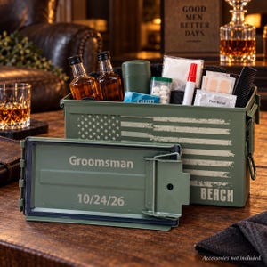 May include: An olive green metal ammunition box featuring a distressed American flag graphic on the side. The lid is detached and displays the text Groomsman and 10/24/26. The box is filled with two small liquor bottles, gum, a red marker, and bandages.