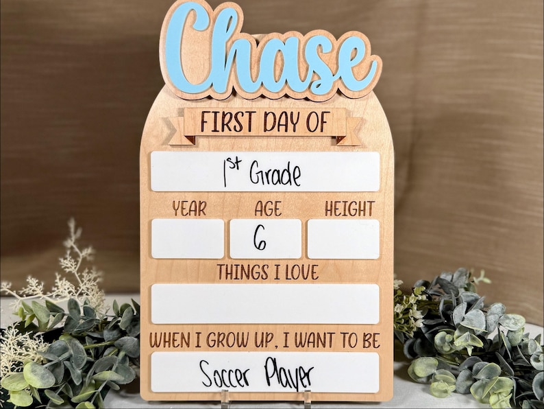 May include: Wooden first day of school sign with the name "Chase" in blue letters. The sign includes spaces to write "1st Grade", age, height, things they love, and "Soccer Player" for what they want to be.