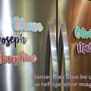 May include: Wooden name magnets in various colors, including blue, teal, and pink glitter, are displayed on a stainless steel refrigerator. The names "Chase", "Joseph", "Josephine", "Olivia", and "Malia" are visible. Text at the bottom reads "Names can also be used as refrigerator magnet".