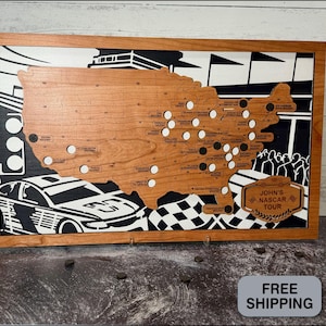 May include: Wooden map of the United States with a cherry finish, framed in a light brown wood. The map features cutouts for NASCAR race locations, with a black and white racing theme in the background. The text "John's NASCAR Tour" is displayed.