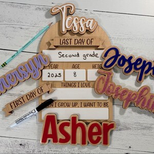May include: Wooden school-themed signs and name cutouts. Includes a sign for "Last Day of Second Grade" with fill-in fields, plus names like Tessa, Joseph, and Asher. A pencil and marker are also present.