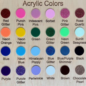 May include: A wooden display board showcasing a variety of acrylic colors. The board features circular color swatches in shades like red, pink, green, blue, and glitter options. Each color is labeled with its name, such as "Red Glitter" and "Neon Green."
