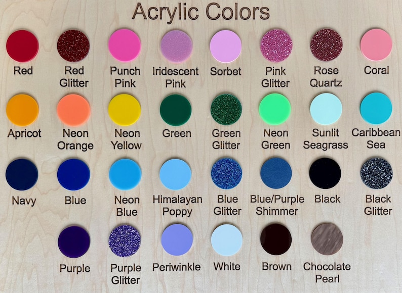 May include: A wooden display board showcasing a variety of acrylic colors. The board features circular color swatches in shades like red, pink, green, blue, and glitter options. Each color is labeled with its name, such as "Red Glitter" and "Neon Green."