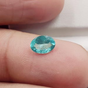 Pode incluir: Uma gema ovalada, cor de &aacute;gua-marinha. A gema &eacute; de um tom vibrante azul-esverdeado, com caracter&iacute;sticas internas vis&iacute;veis. A pedra &eacute; colocada sobre um fundo neutro, destacando sua cor e clareza. Esta gema pode ser usada em joias.