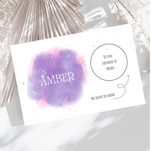 May include: A purple and pink watercolor background with white glitter and the name "AMBER" in white text. A circle with the text "YOUR MESSAGE HERE." and an arrow pointing to the text "SCRATCH HERE" below.