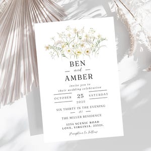May include: A white wedding invitation with a floral design at the top. The invitation reads "Ben and Amber invite you to their wedding celebration October 25, 2025 Saturday Six Thirty in the Evening at The Miller Residence 1234 Scenic Road Love, Virginia. 23321. Reception to Follow."