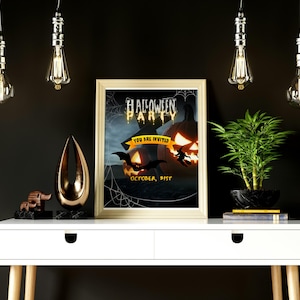 Puede incluir: Un póster enmarcado de Halloween Party con una calabaza, murciélagos y el texto "You are invited". El póster está sobre una mesa blanca con objetos decorativos y una planta. Cuatro bombillas Edison cuelgan del techo.