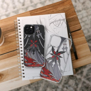 May include: Two clear phone cases with black and red floral designs. The cases are on a notebook with a pencil and a coffee cup.