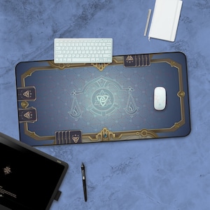 Pode incluir: Um tapete de rato para jogos azul e dourado com um padrão geométrico e um símbolo estilizado no centro. O tapete de rato está sobre uma superfície azul com um teclado branco, uma caneta branca e um caderno branco.