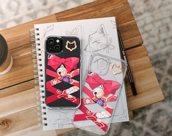 May include: Black iPhone case with a red bow design, gold accents, and a black background. A clear phone case with the same design is next to it on a spiral notebook. A pen and a cup are also visible.