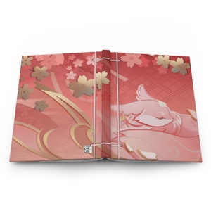 May include: An open book with a red and gold patterned cover. The cover features a pink bird with a white wing and a floral design. The book is bound with a string.