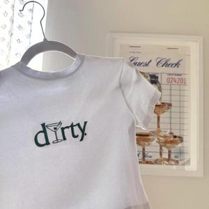 May include: White cropped t-shirt with a green graphic of a martini glass and the word "dirty" printed on the front.