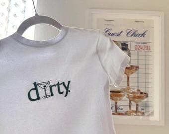 May include: White cropped t-shirt with a green graphic of a martini glass and the word "dirty" printed on the front.
