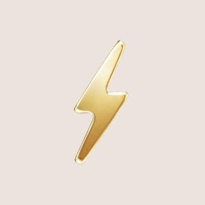 May include: A polished gold-tone metal pin shaped like a lightning bolt. The object features a smooth, reflective surface with clean, sharp edges and a classic zig-zag silhouette, designed as a decorative accessory for clothing or fabric items.