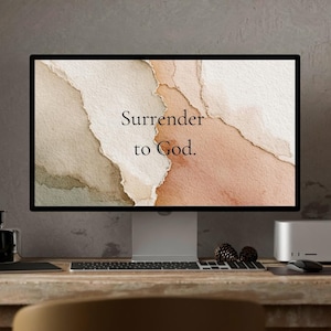 May include: A computer monitor displays a watercolor-style image with a blend of beige, brown, and peach tones. The text "Surrender to God" is centered on the screen. The monitor sits on a wooden desk with a keyboard, mouse, and other office accessories.