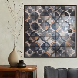 May include: Square framed wall art featuring a geometric pattern of overlapping circles in shades of blue, gray, and bronze. The artwork is composed of individual square tiles. A neutral-toned vase and a small black vase sit on a wooden surface.