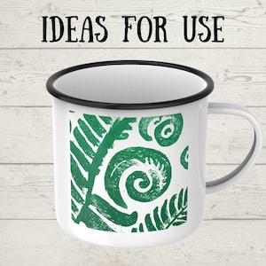 May include: White enamel mug with a black rim and handle. The mug features a green fern design and the text "IDEAS FOR USE" in black. The mug is likely used for beverages.