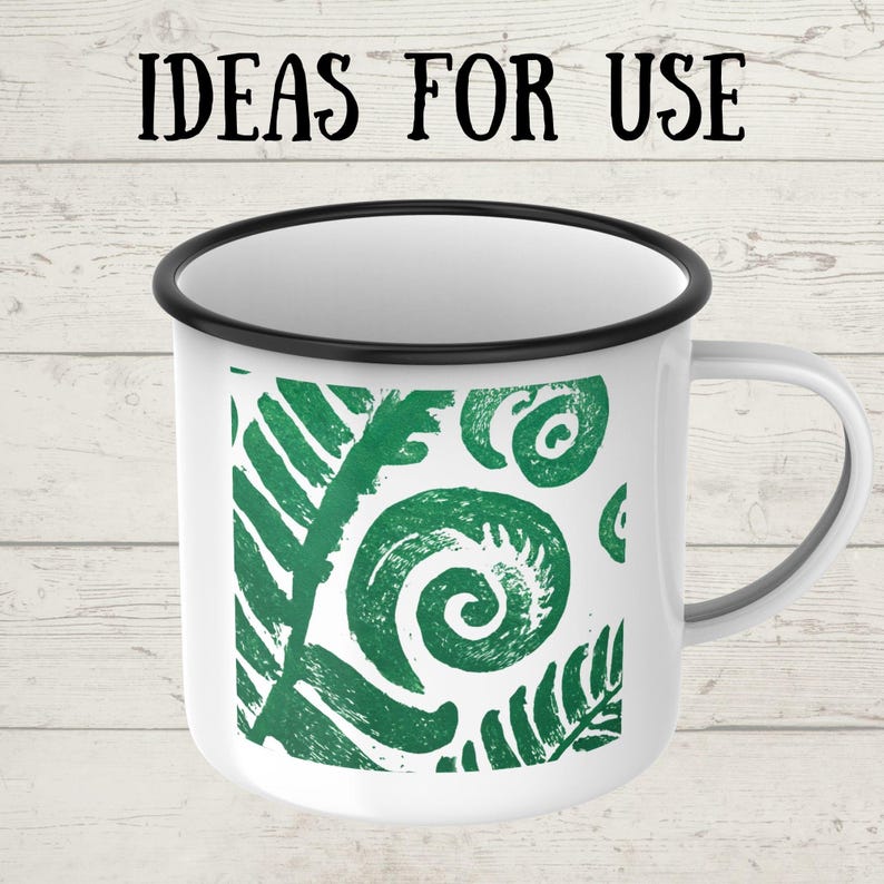 May include: White enamel mug with a black rim and handle. The mug features a green fern design and the text "IDEAS FOR USE" in black. The mug is likely used for beverages.