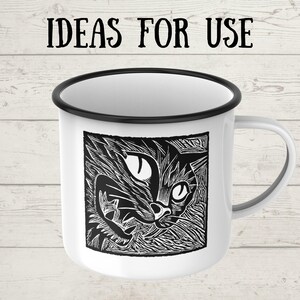 May include: White enamel mug with a black rim and handle. The mug features a black and white linocut print of a cat's face. The text "IDEAS FOR USE" is printed above the cat image.