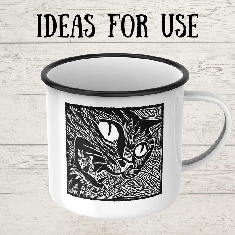 May include: White enamel mug with a black rim and handle. The mug features a black and white linocut print of a cat's face. The text "IDEAS FOR USE" is printed above the cat image.