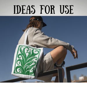 May include: A white tote bag with a green botanical design. The bag has a rectangular print of stylized leaves and swirls. The words "IDEAS FOR USE" are printed in black at the top of the image. The bag is carried by a person wearing a grey sweatshirt and shorts.