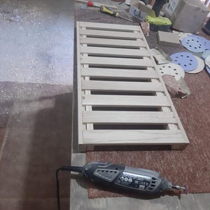 May include: A rectangular wooden slatted rack featuring light-colored natural wood planks arranged in a parallel pattern. The structure is composed of multiple horizontal slats secured to a frame, creating a grid-like surface for various utility purposes.