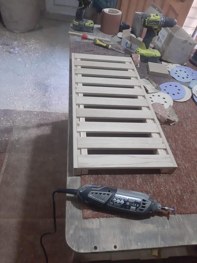 May include: A rectangular wooden slatted rack featuring light-colored natural wood planks arranged in a parallel pattern. The structure is composed of multiple horizontal slats secured to a frame, creating a grid-like surface for various utility purposes.