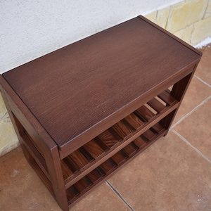 May include: A rectangular dark brown wooden shoe rack featuring a solid flat top surface and two lower slatted shelves for storage. The unit is constructed with sturdy vertical side panels and horizontal supports, showcasing a natural wood grain finish.