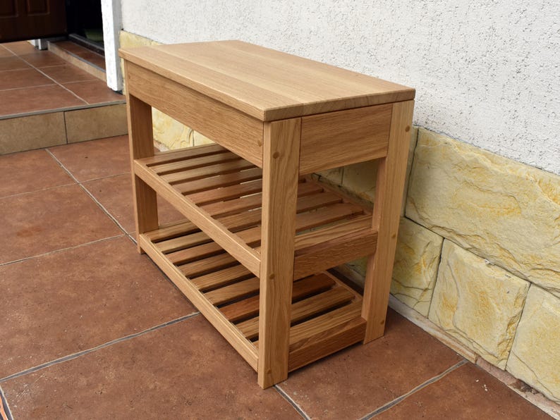May include: A light brown wooden console table featuring a solid rectangular top surface and two lower slatted shelves. The structure is supported by four vertical legs, showcasing a natural wood grain finish throughout the entire piece of furniture.