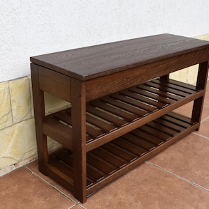 May include: A rectangular wooden shoe rack with a dark brown finish. The piece features a solid flat top surface and two lower shelves constructed with horizontal slats. The frame is composed of four vertical legs connected by horizontal supports.