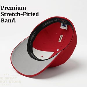 May include: A red baseball cap with a grey underside of the brim and a black interior sweatband featuring the text Flexfit. The cap includes a white interior panel and a size tag reading S-M. Text in the image reads Premium Stretch-Fitted Band.