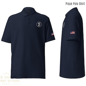 May include: Navy blue pique polo shirt with a white embroidered design of a circle with stars and the numbers 45, 47. The shirt also has a small American flag on the sleeve.