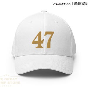以下が含まれることがあります： ゴールドの数字「47」が入った白いFlexfitウールコームキャップ。キャップはカーブしたつばと構造化されたフィット感があります。「FLEXFIT | WOOLY COMBED CAP」の文字がキャップの上部にプリントされています。「WHITE」の文字が右下にプリントされています。
