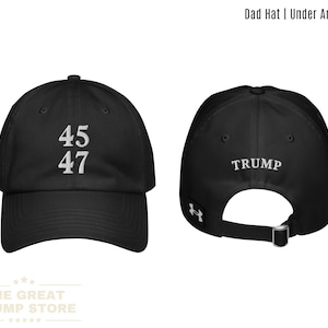 Puede incluir: Gorra de papá negra con texto bordado en blanco "45 47" en la parte delantera y "TRUMP" en la parte posterior. La gorra tiene un logotipo de Under Armour negro en el lateral.