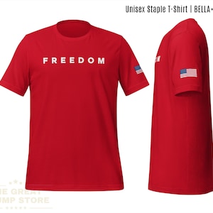 May include: Red unisex t-shirt with the word "FREEDOM" in white block letters across the chest. The sleeve features a small American flag. The shirt is a Bella+Canvas staple.