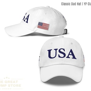 Puede incluir: Gorra de béisbol blanca con la palabra "USA" en letras de bloque azul marino. La bandera estadounidense está bordada en el lateral. El texto "Classic Dad Hat | YP Classics®" está en la parte superior.