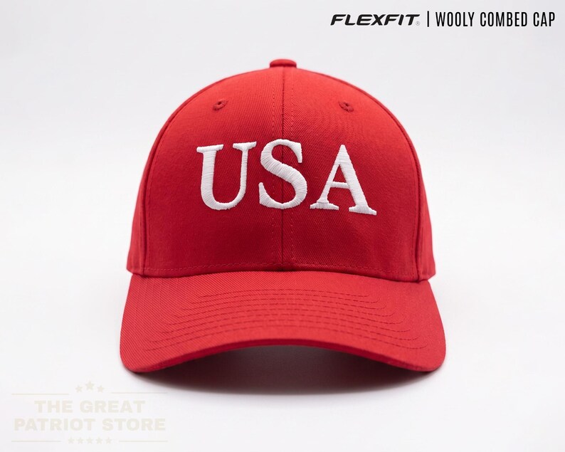 May include: A bright red baseball cap featuring the text USA embroidered in white on the front. The cap is labelled as a Flexfit Wooly Combed Cap. The design includes a structured crown and a curved brim, presenting a clean and simple aesthetic.