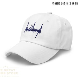 May include: White Classic Dad Hat with a curved brim. The hat features a navy blue embroidered signature on the front. The text "Classic Dad Hat | YP Classics®" is printed at the top. The text "WHITE" is printed at the bottom.