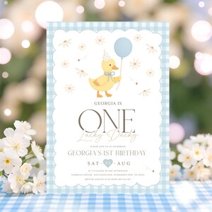 May include: A light blue and white gingham patterned invitation for a first birthday. The invitation features a cartoon duck holding a blue balloon. The text reads "GEORGIA IS ONE Lucky Ducky" and details for the party.