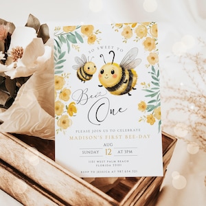 Op de afbeelding: Een witte uitnodigingskaart met een gele en groene bloemenrand. De kaart heeft een cartoon-bij met de tekst "So Sweet To Bee One" en de woorden "Please join us to celebrate Madison's First Bee-Day". De datum en tijd van het evenement zijn vermeld als "Zondag 12 augustus om 15:00 uur". De locatie is vermeld als "1101 West Palm Beach, Florida 33101". De RSVP-informatie is "RSVP naar Jessica op 987.654.321".