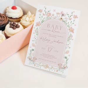 May include: A pink and white baby shower invitation with a floral design. The text reads "Baby in Bloom" and includes the name "Kelsey Jackson", the date "July 17", and the time "1 PM".