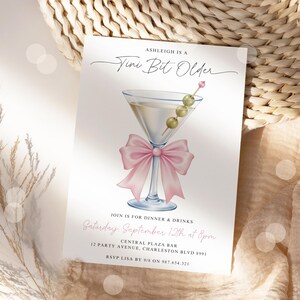May include: A white invitation card with a martini glass illustration. The martini glass has a pink bow and olives. Text reads "Ashleigh is a Vini Bit Older" and details for a dinner party.
