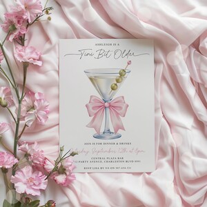 May include: A party invitation with a martini glass illustration and a pink bow. The text reads "Ashleigh is a Tini Bit Older" and includes event details: dinner and drinks, date, time, location, and RSVP information.