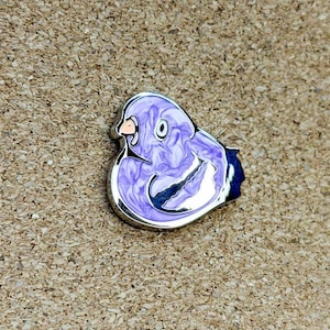 May include: A metal enamel pin shaped like a stylized bird in profile. The pin features a swirling lavender and white marbled pattern with a silver-toned metallic outline. It has a small, distinct eye and a beak detail, with a dark blue wing section.
