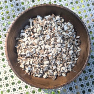 May include: A wooden bowl filled with dried, light brown and white root pieces. The bowl is on a white and green woven surface.