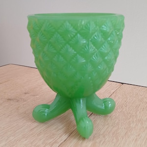 May include: A bright green glass bowl featuring a textured pineapple-inspired diamond pattern on the exterior. The bowl is supported by three curved, integrated feet that extend from the base, creating a raised, tripod-style structure.